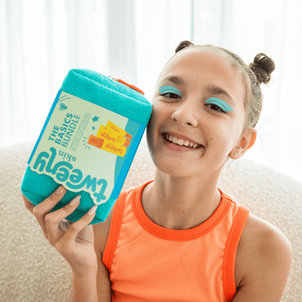 Happy tween girl holding the Tweeny Skin Basics Bundle — a skincare starter pack designed for tweens and teens. Featuring gentle, fragrance-free essentials in bright, fun packaging, this award-winning bundle is perfect for young, sensitive skin and helps build confident skincare habits from the start.