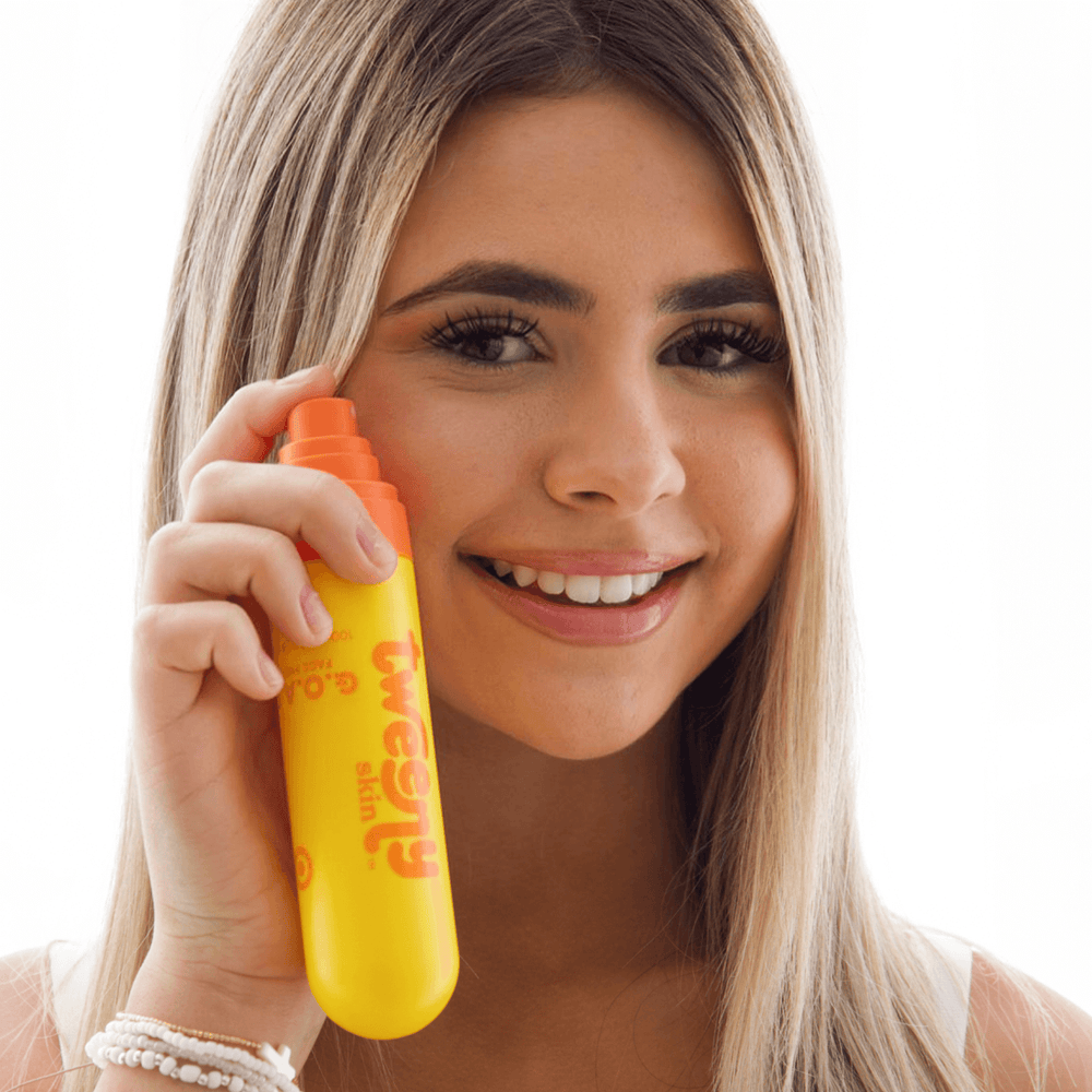 Smiling teen girl holding Tweeny Skin G.O.A.T. Hypochlorous Face Mist bottle near her cheek, ready to spray.