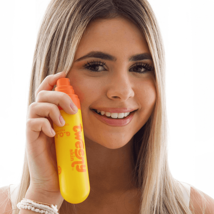 Smiling teen girl holding Tweeny Skin G.O.A.T. Hypochlorous Face Mist bottle near her cheek, ready to spray.